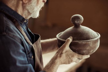 Senior potter in apron examining ceramic bowl at workshop clipart