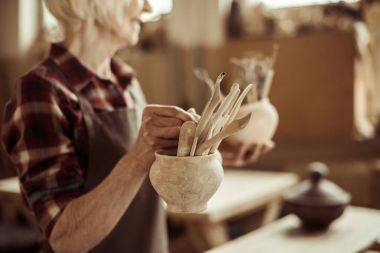 Senior woman holding bowls with pottery tools at at workshop clipart