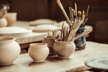 Close up of paint brushes with pottery tools in bowls on table