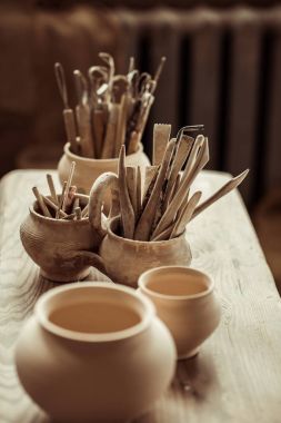 Close up of paint brushes with pottery tools in bowls on table clipart