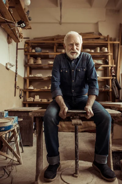 Front view of senior man sitting on table and working on pottery wheel — Free Stock Photo