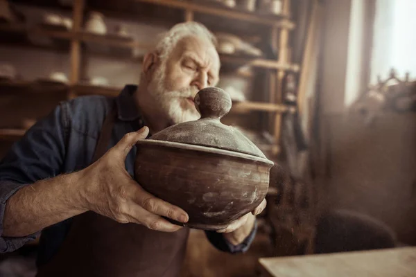 Alfarero senior en delantal examinando tazón de cerámica en el taller — Foto de Stock