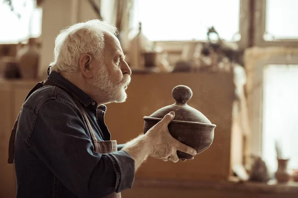 Senior potter i förklädet undersöker keramikskål på verkstad — Stockfoto