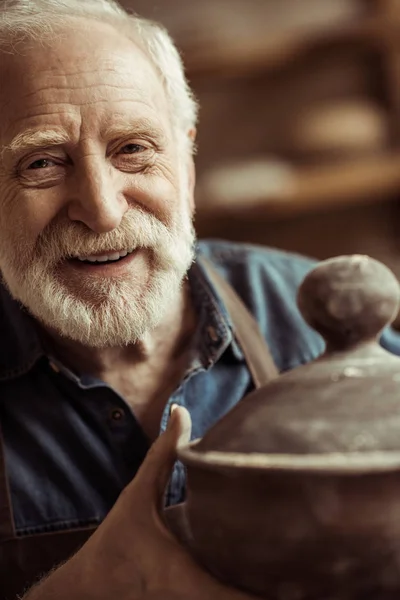 Senior pembuat tembikar di celemek memeriksa mangkuk keramik di bengkel — Foto Stok Gratis
