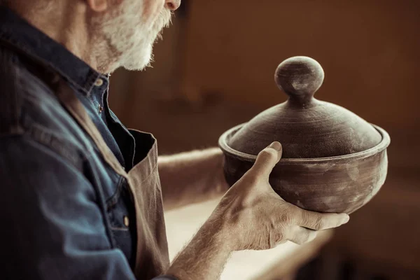 Potier senior dans un tablier examinant un bol en céramique à l'atelier — Photo