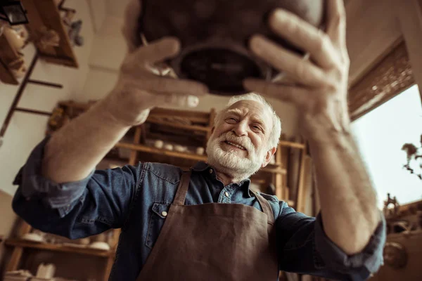 Vedoucí potter v zástěře zkoumání keramické mísy na workshopu — Stock fotografie