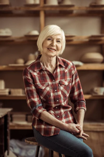 Vooraanzicht van senior vrouw zit op stoel tegen planken met aardewerk goederen — Gratis stockfoto