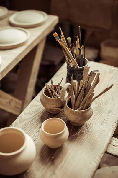 Close up de pincéis de tinta com ferramentas de cerâmica em tigelas na mesa — Fotografia de Stock