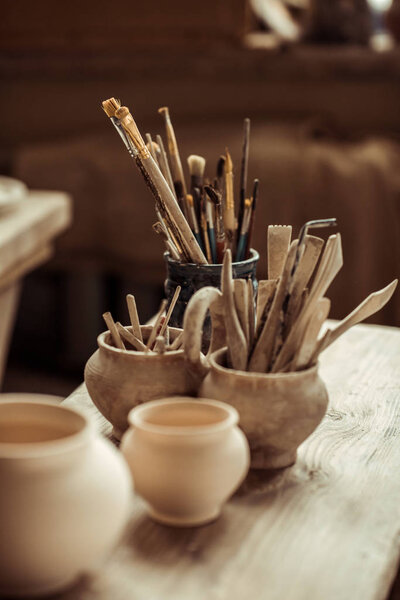 Close up of paint brushes with pottery tools in bowls on table