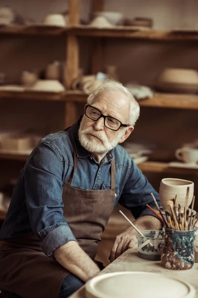 Üst düzey potter masada oturan ve Atölyesi'nde hayal önlük — Stok fotoğraf