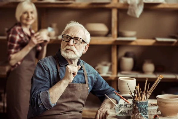 Senior potter sitting at table and thinking with senior woman at workshop — Stock Photo, Image