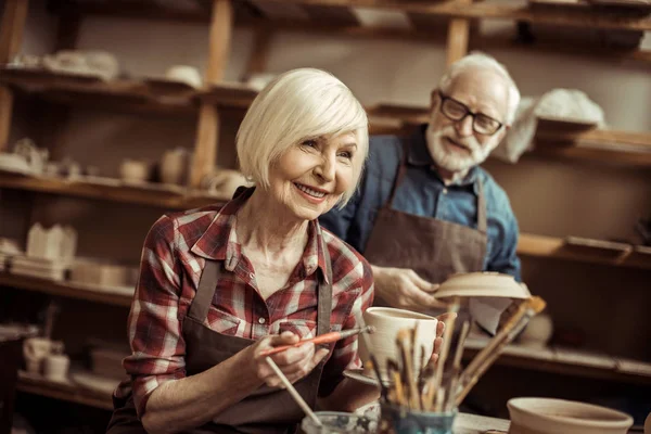 Женщина рисует глиняный горшок со старшим гончаром в мастерской — стоковое фото