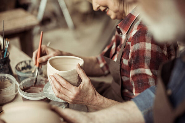 Вид сбоку на женщину, рисующую горшок с когтями в мастерской
