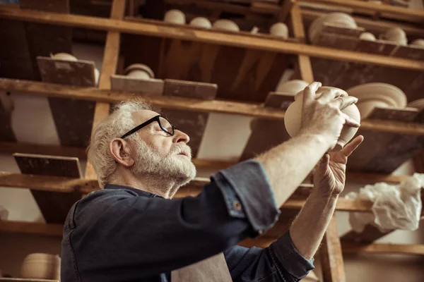 Vedoucí potter v zástěře a brýle zkoumání keramické mísy na workshopu — Stock fotografie