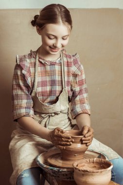 Front view of little girl making pottery on wheel at workshop clipart