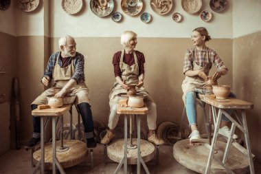 Grandmother and grandfather with granddaughter making pottery at workshop clipart