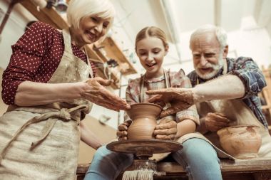 Grandmother and grandfather with granddaughter making pottery at workshop clipart