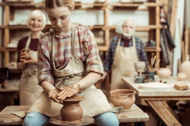 Grandmother and grandfather with granddaughter making pottery at workshop clipart