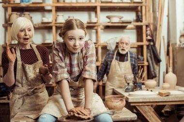 Grandmother and grandfather with granddaughter making pottery at workshop clipart