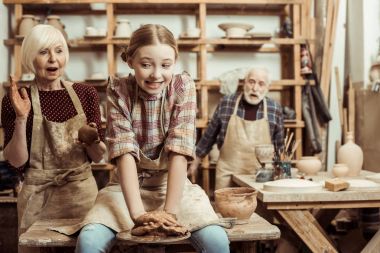 Grandmother and grandfather with granddaughter making pottery at workshop clipart