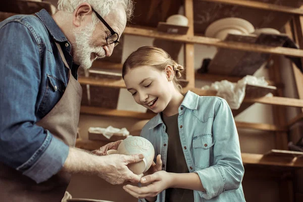 Онука і дідусь тримають і вивчають глиняні вироби — стокове фото
