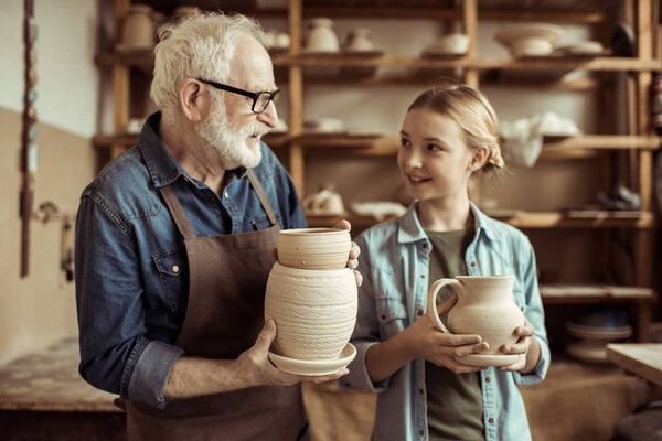 Granddaughter and grandfather holding and examining clay goods