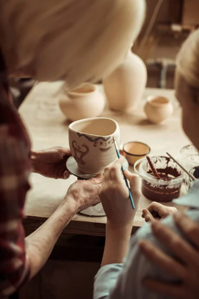 Close up of girl painting clay pot and grandparents helping at workshop — Stock Photo, Image