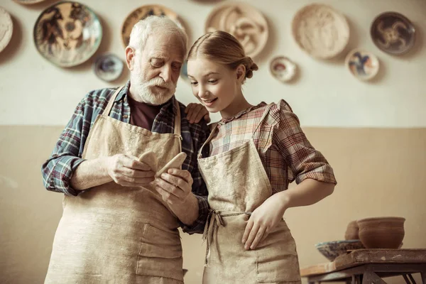 Front view of senior potter showing details to his granddaughter while standing at workshop — Stock Photo, Image
