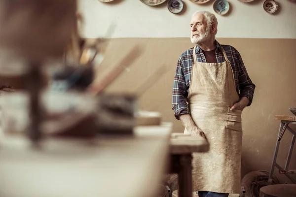 Front view of senior potter in apron standing at workshop — Stock Photo, Image