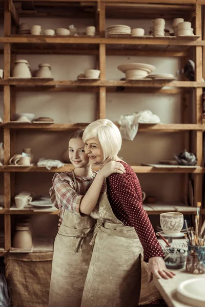 Granddaughter hugging her grandmother while they standing in aprons at workshop — Free Stock Photo