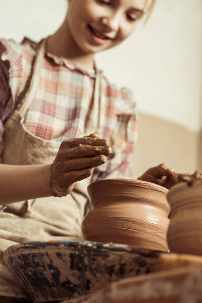 Close up of little girl making pottery on wheel at workshop