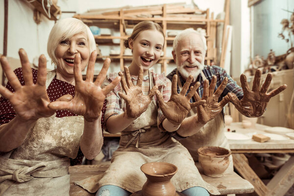 Grandmother and grandfather with granddaughter showing hands in clay in workshop
