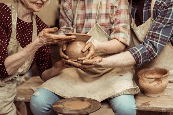 Обрезанное изображение бабушки и дедушки с внучкой, делающей керамику в мастерской — стоковое фото