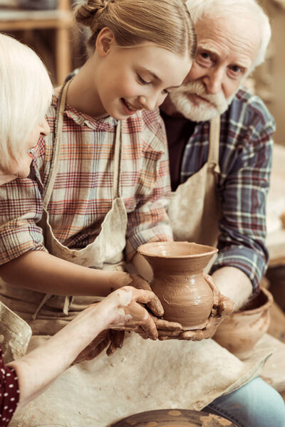 Grandmother and grandfather with granddaughter making pottery at workshop