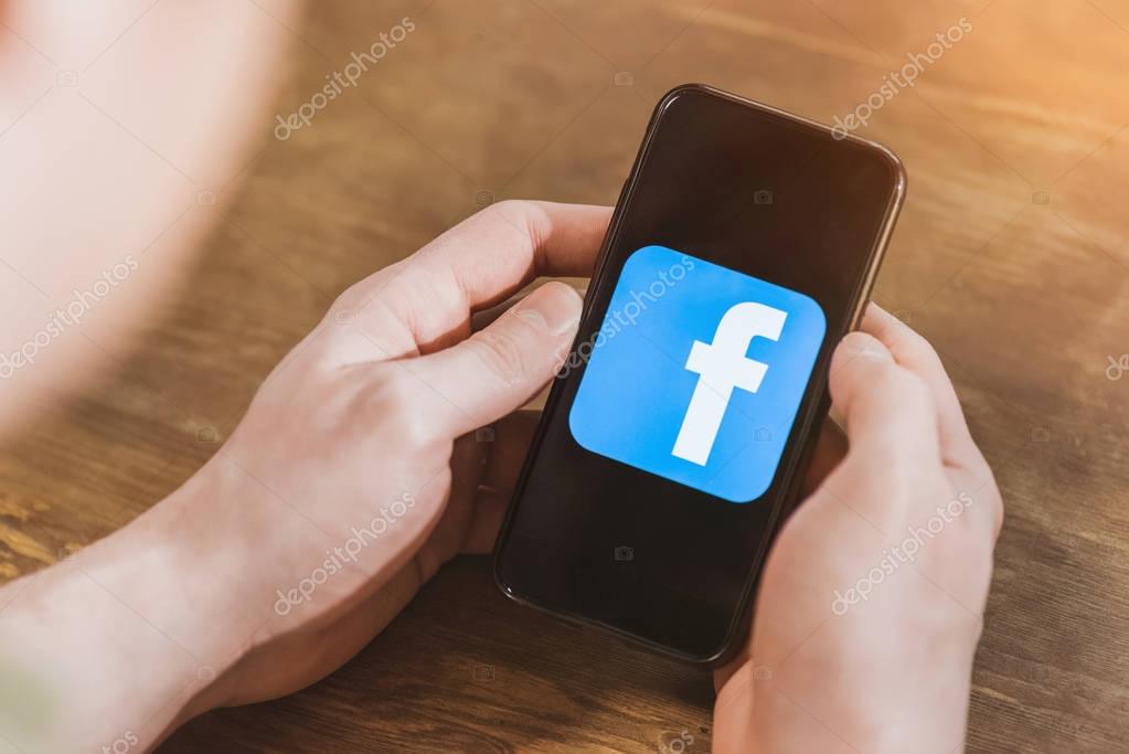 Man using smartphone with facebook logo icon on screen