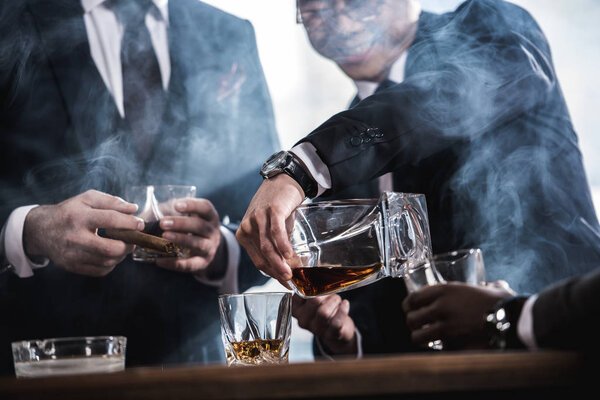 обрезанный вид на бизнес-команду, проводящую время, курящую сигары и пьющую виски
