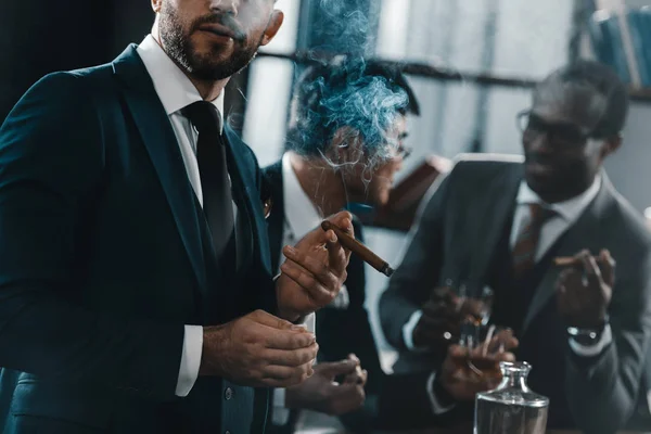 Businessman smoking cigar with multicultural business team spending time behind — Stock Photo, Image