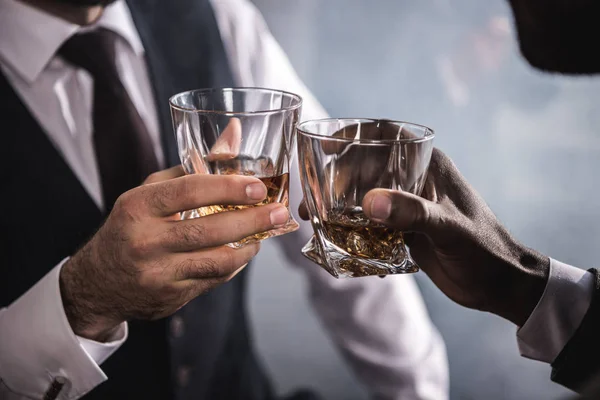 Close-up partial view of two men in formal wear clinking whiskey glasses — Stock Photo, Image