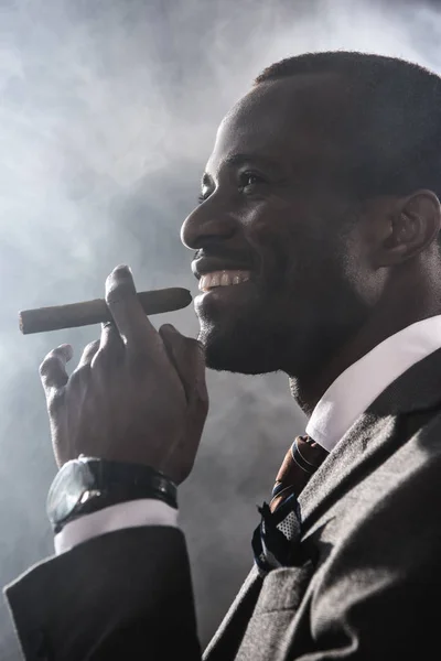 Side view of smiling confident man smoking cigar indoors — Stock Photo, Image