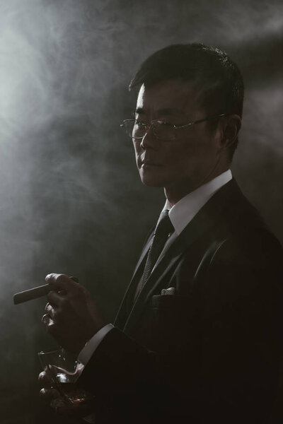 портрет уверенного азиатского бизнесмена в костюме со стаканом сигары для курения виски
 