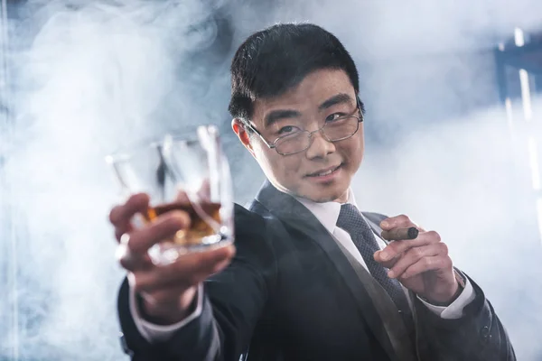 Close-up view of confident asian businessman drinking whiskey and smoking cigar — Stock Photo, Image