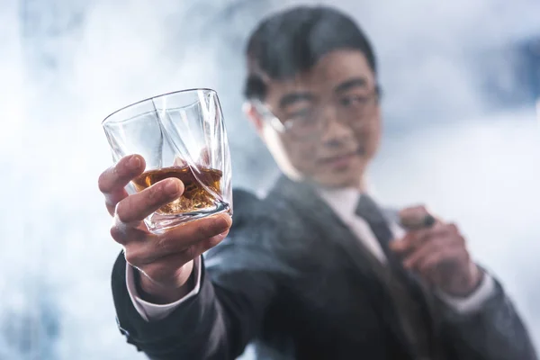 Close-up view of confident asian businessman drinking whiskey and smoking cigar — Stock Photo, Image