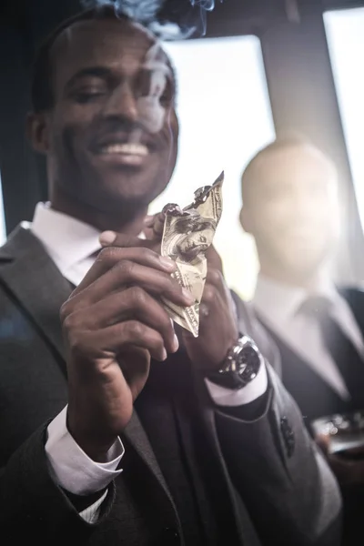 Close-up view of confident smiling businessman lighting cigar with dollar banknote — Free Stock Photo