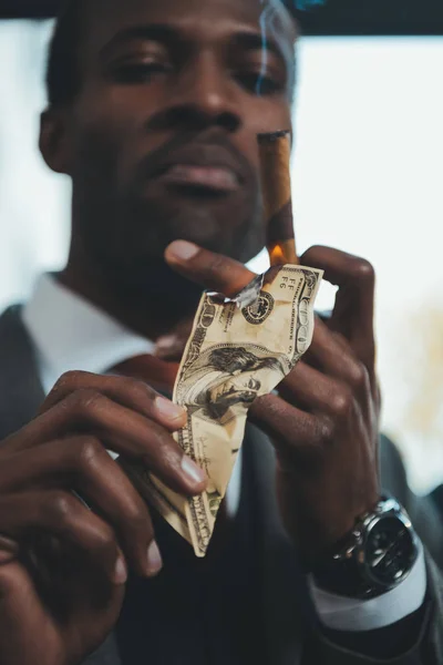 Confident african american businessman smoking cigar and burning dollar banknote — Stock Photo, Image