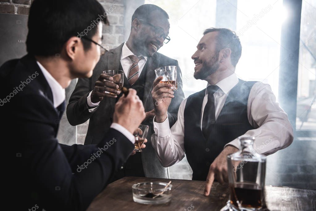 Multiethnic group of businessmen smoking and drinking whisky indoors, multicultural business team