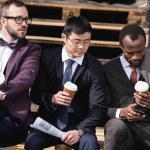 Jóvenes hombres de negocios multiétnicos en ropa formal sentados en la pausa de café al aire libre, reunión del equipo de negocios