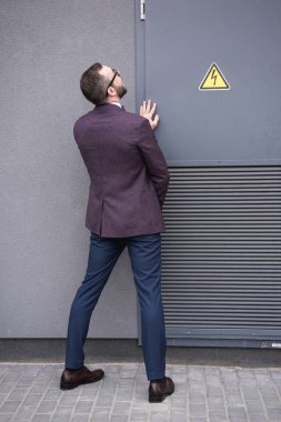 back view of stylish businessman peeing on street near transformer  clipart
