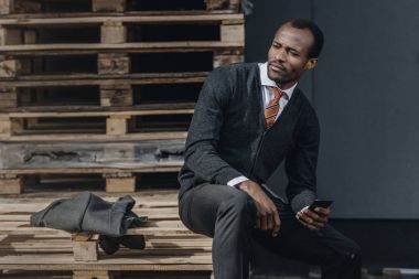 Smartphone kullanarak ve açık havada oturma yorgun şık Afrikalı-Amerikalı işadamı 