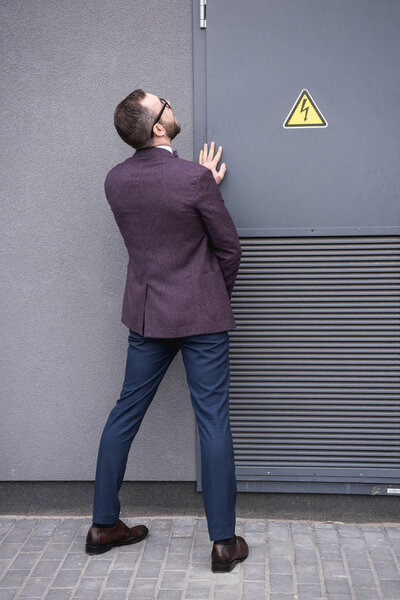 back view of stylish businessman peeing on street near transformer 