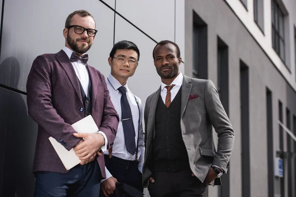 Jóvenes y elegantes hombres de negocios multiétnicos en ropa formal posando al aire libre, reunión de equipo de negocios — Foto de Stock